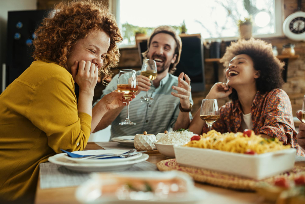 3 pessoas sentadas em uma mesa comendo felizes, compartilhando refeições