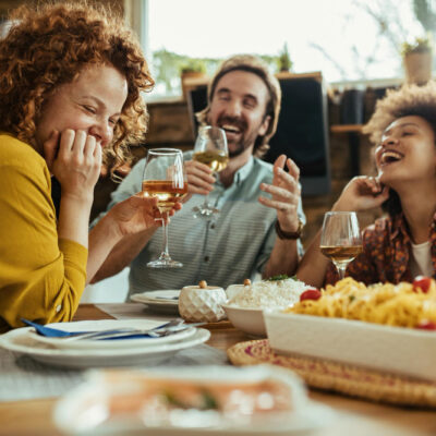 3 pessoas sentadas em uma mesa comendo felizes, compartilhando refeições